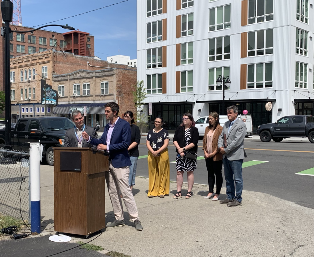 Spokane, WA Councilperson Zack Zappone at lectern in front of new mixed-use building