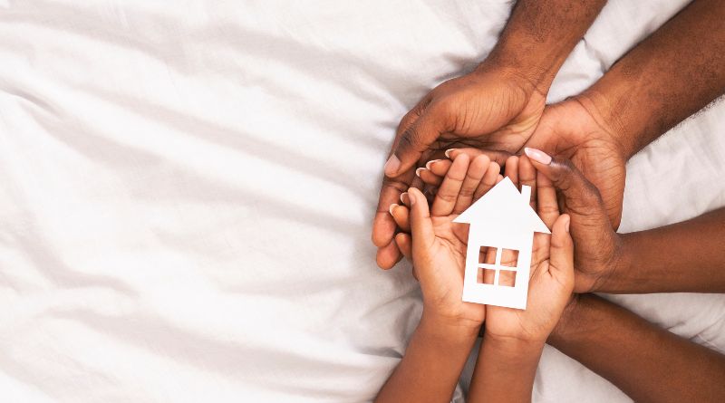 Black family of three holding paper house figure in hands