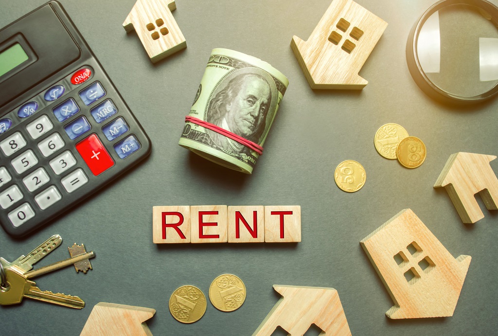 Table with wooden houses, calculator, coins, magnifying glass with the word Rent.