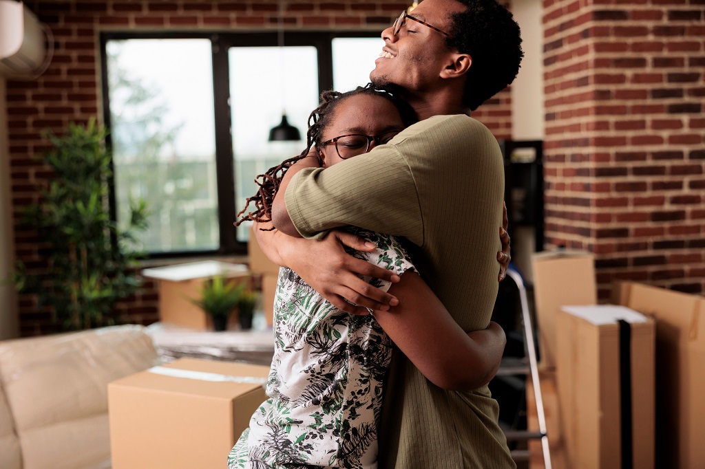 African American couple sharing hug and enjoying property relocation, having romantic moment after moving in new house together. Hugging and celebrating life event in rented flat.