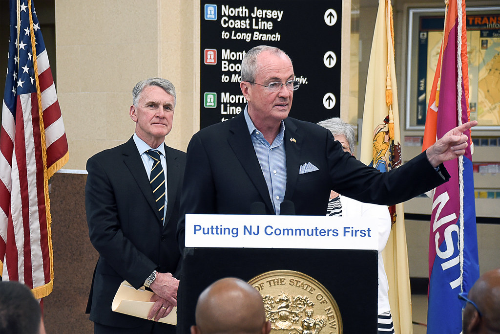 Governor Phil Murphy speaking behind a podium that states "Putting NJ Commuters First"