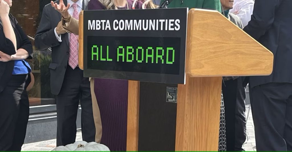 A podium that says ”MBTA Communities. All Aboard.”