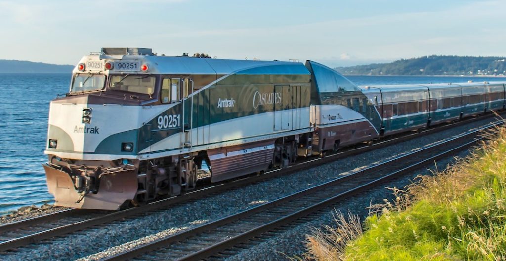 Amtrak Cascades train traveling along a body of water. 