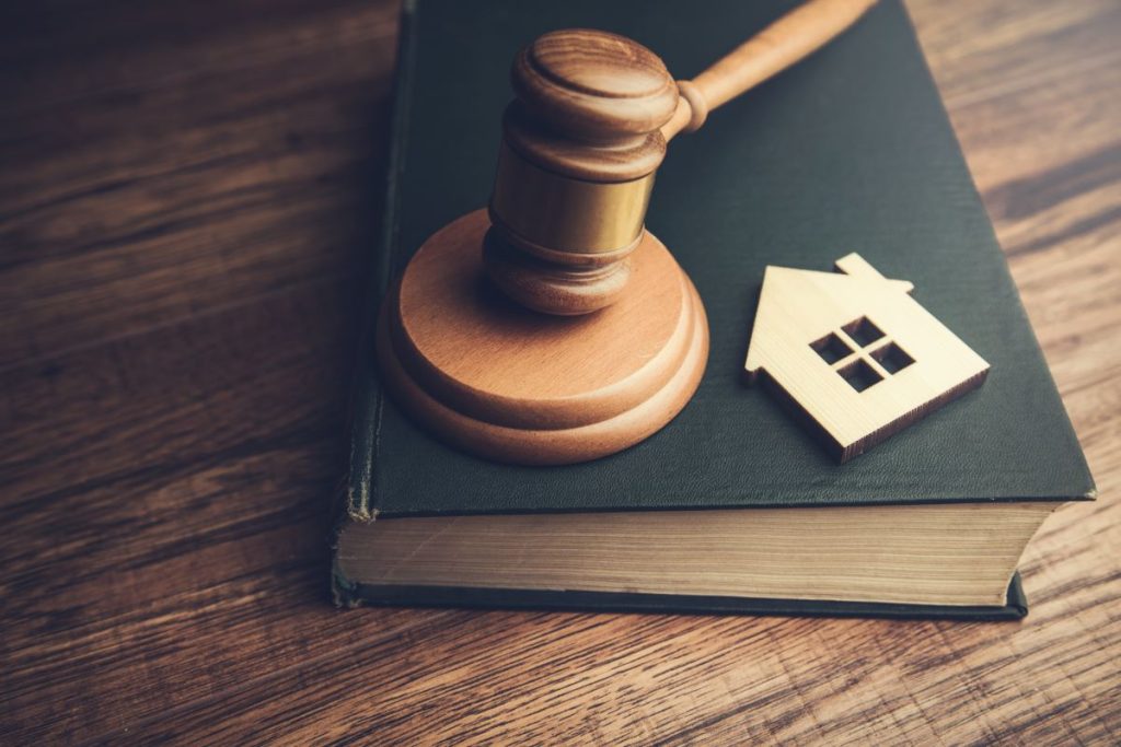 A legal gavel resting on a law book and next to a miniature house.