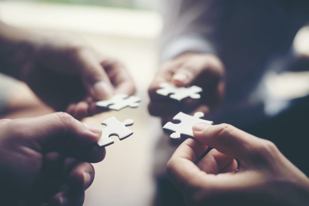 Multiple hands holding puzzle pieces together.