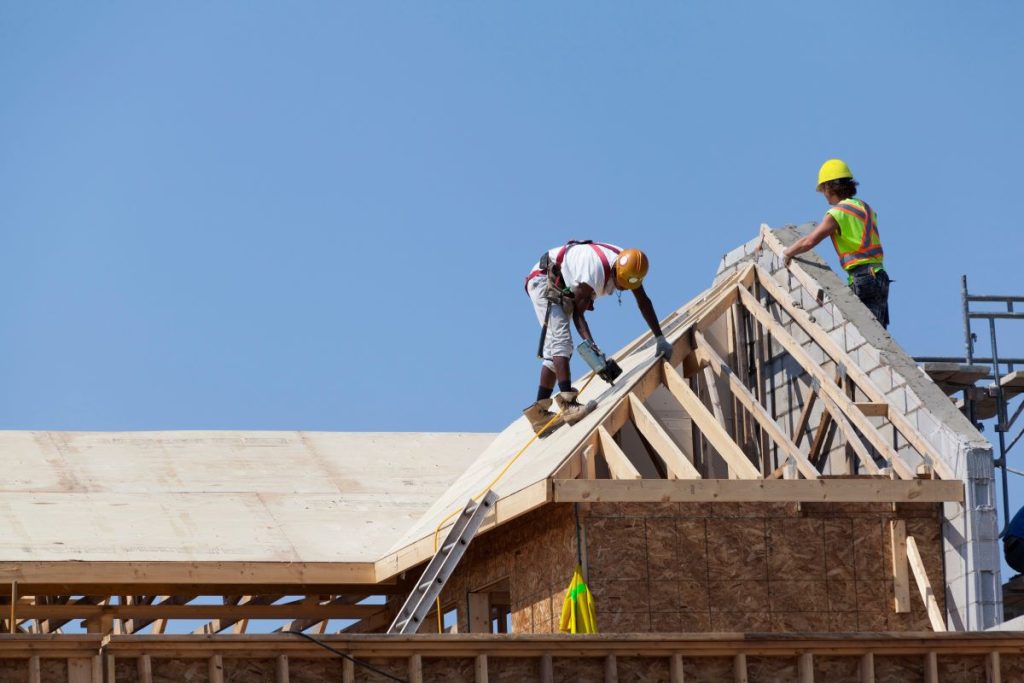 Two carpenters building a roof on a townhome.