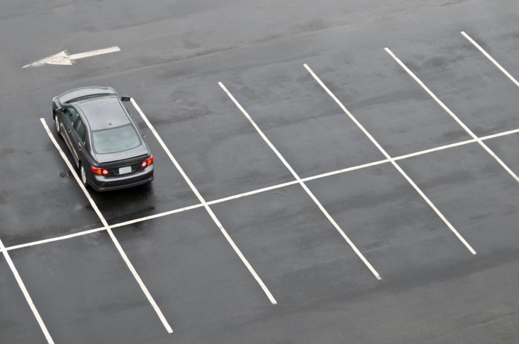 A large parking lot with only one car in a parking space.