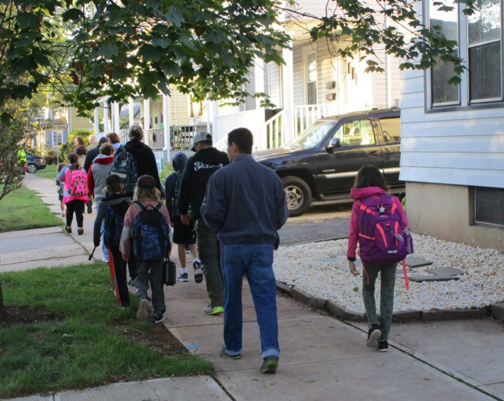 Parents and children walking to school on a sidewalk.