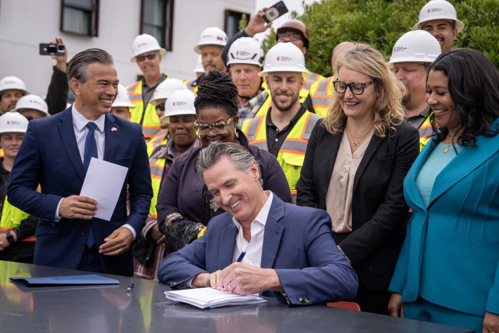 California Governor Gavin Newsom signing legislation in front of construction workers.