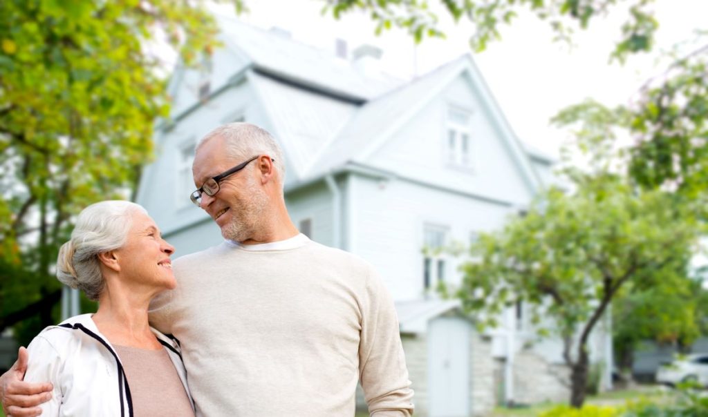 Two older adults standing in front of their house