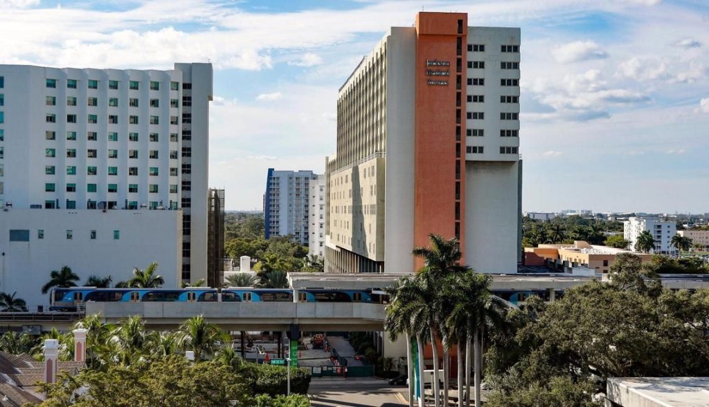 UHealth-Jackson Metrorail station in Miami, with the two towers that will be demolished for the redevelopment in the background. In the foreground is a train.