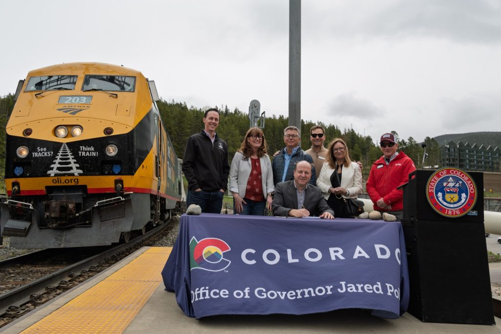 Governor Jared Polis signing HB26-1065 into law. He and other officials are sitting in front of a train.