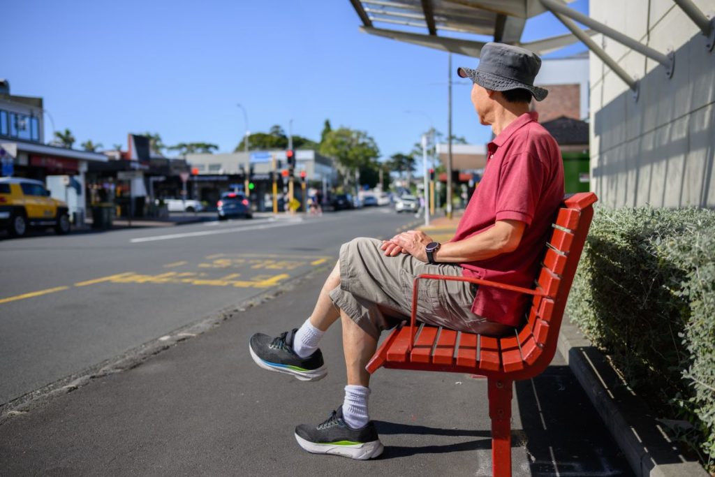 Older man sitting on a bench at a bus stop