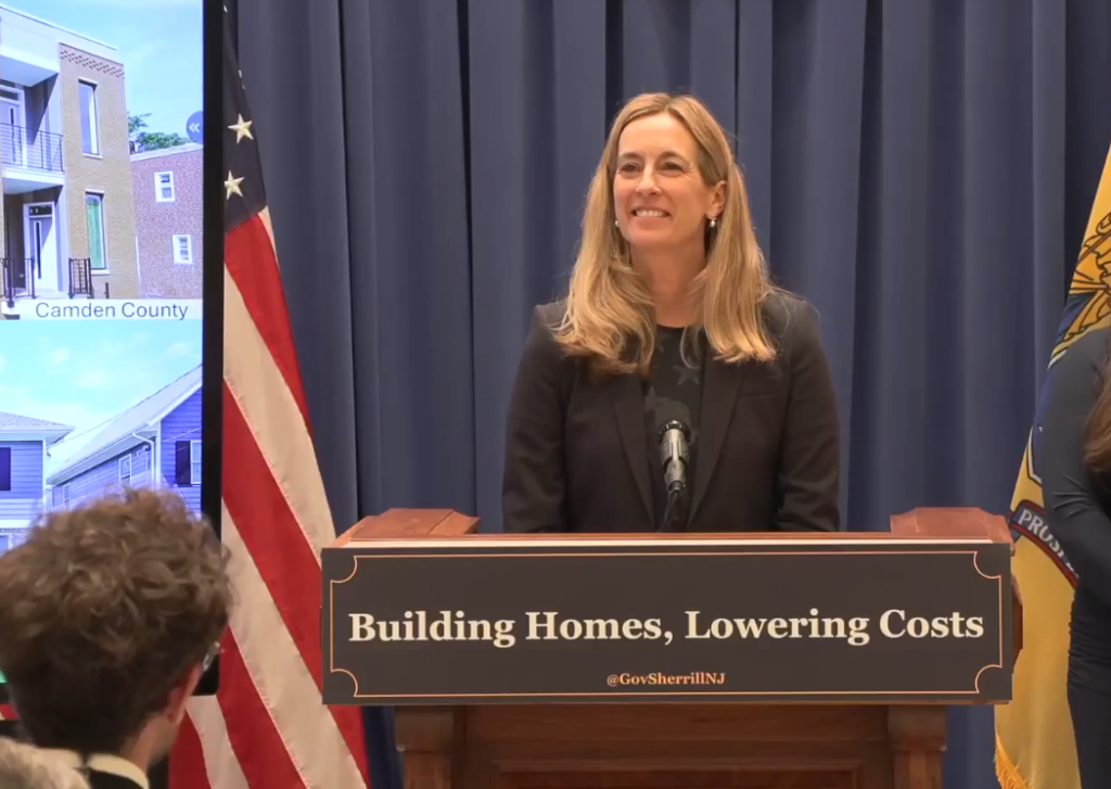 Mikie Sherrill delivering a speech in front of a podium that says "Building Homes, Lowering Costs"