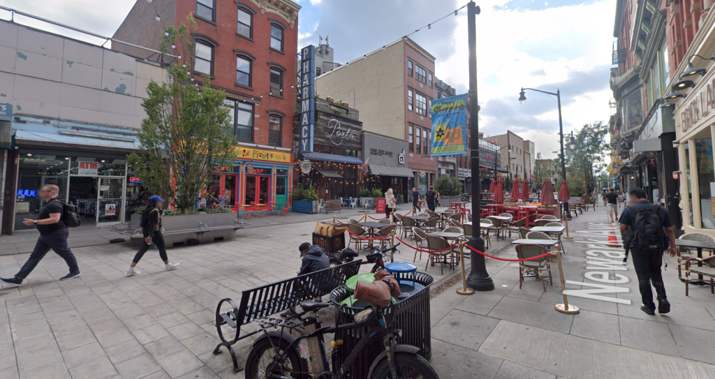Pedestrian plaza in Jersey City. There are people walking and frequent seating.