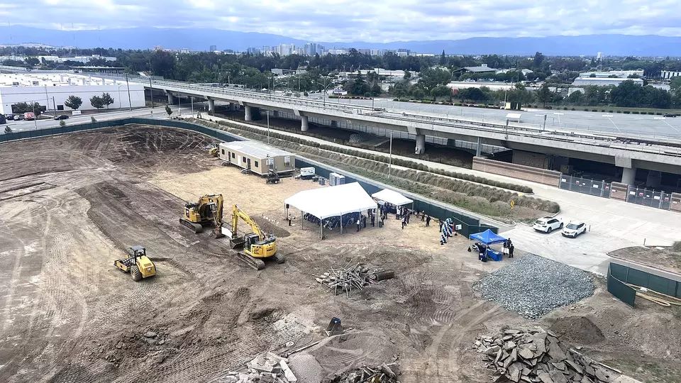 Aerial photo of the construction site that will soon be home to RISE, an affordable housing development next to the Berryessa/North San José BART Station, with the San José skyline in the background.